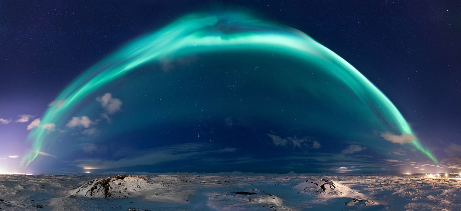 A bright green arc of the northern lights spanning a starry sky above a snowy Icelandic landscape